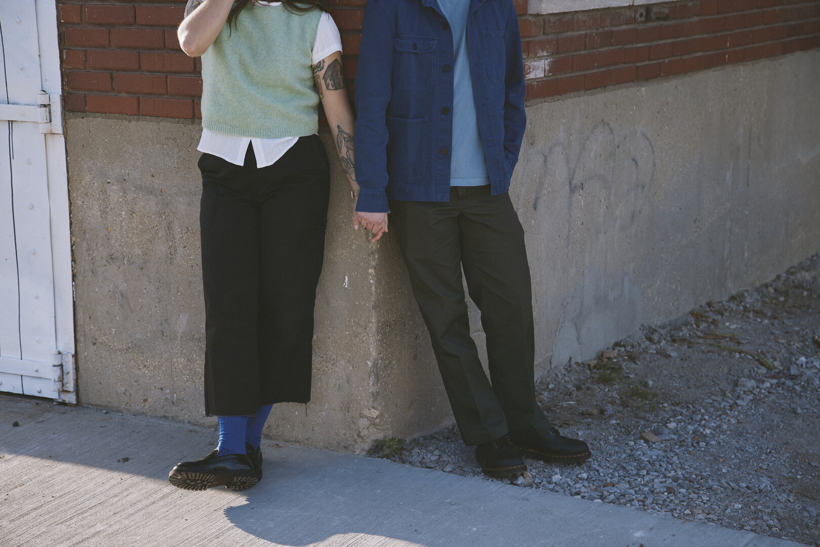 Andy and Brit holding hands against a concrete wall