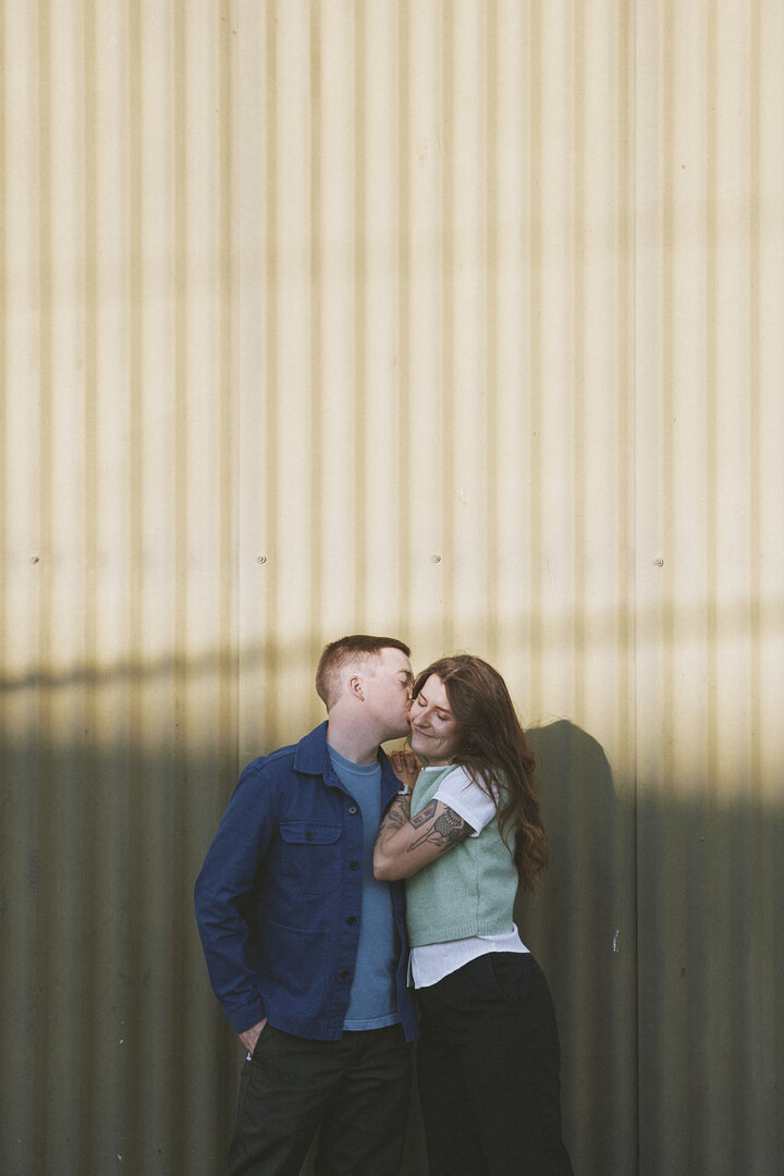 Andy and Brit embracing by metal wall